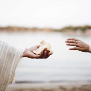 Closeup shot of a person wearing a biblical robe giving bread to another person